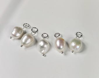 May include: Five white pearl charms with silver jump rings. The pearls are different sizes and shapes.