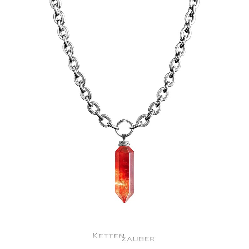 May include: A silver chain necklace with a red crystal pendant in the shape of a long, pointed, geometric shape.