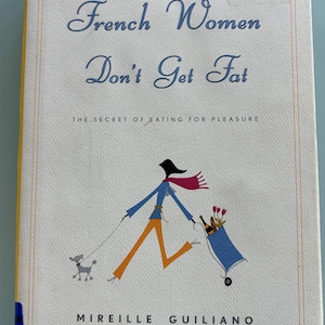 May include: Book cover with a blue and white illustration of a woman walking a dog and pushing a shopping cart. The title is "French Women Don't Get Fat: The Secret of Eating for Pleasure" by Mireille Giuliano.