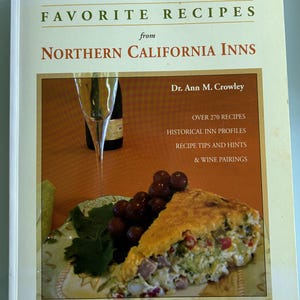 May include: A cookbook titled "Favorite Recipes from Northern California Inns" by Dr. Ann M. Crowley. The cover features a slice of quiche, grapes, and a wine glass. The book promises over 270 recipes, historical inn profiles, recipe tips, and wine pairings.