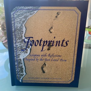 May include: A blue hardcover book titled "Footprints: Scripture with Reflections Inspired by the Best-Loved Poem" by Margaret Fishback Powers. The cover features a photograph of footprints in the sand with a wave crashing in the background.