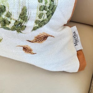 Pu&ograve; includere: Primo piano di un cuscino decorativo con un motivo floreale e di foglie. Il cuscino presenta uno sfondo bianco con accenti ricamati verdi, rosa e marroni. Il cuscino ha un'etichetta Martha Stewart.