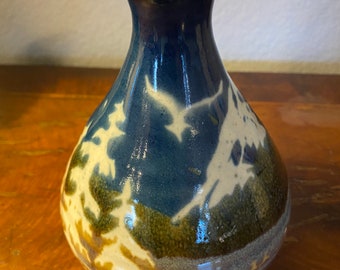 Op de afbeelding: Een kleine, blauwe en witte keramische vaas met een bruine en groene glazuur. De vaas heeft een rond lichaam en een smalle hals.
