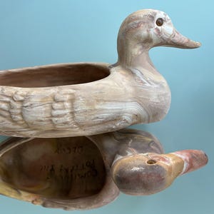 May include: A ceramic duck planter with a marbled brown and white finish. The planter has a large opening for planting and the duck's head is tilted to the side. The planter is signed "Country Pottery Inc. Decor".