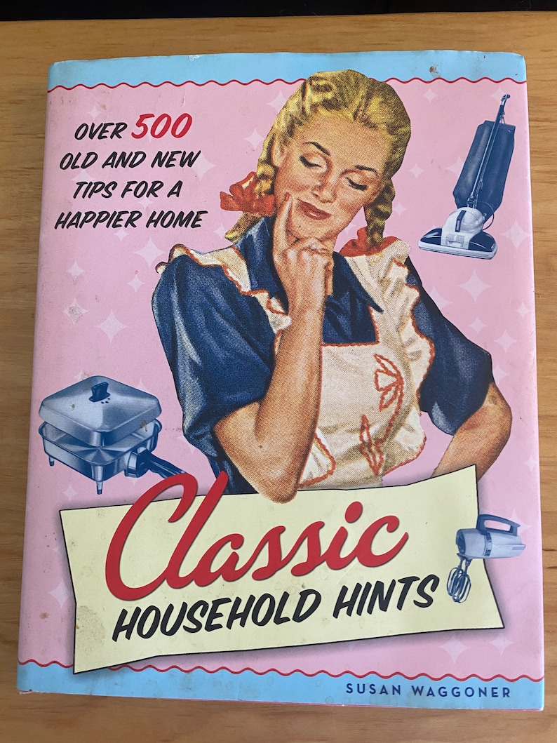 Pode incluir: Uma capa de livro de estilo vintage com fundo rosa e uma mulher em um vestido azul e branco. O t&iacute;tulo do livro &eacute; "Classic Household Hints" e o subt&iacute;tulo &eacute; "Over 500 Old and New Tips for a Happier Home".