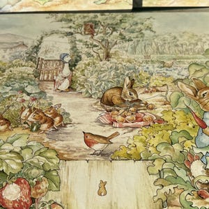 May include: A rectangular placemat featuring a detailed watercolor illustration of a garden scene with multiple rabbits, a duck, and birds. The scene includes a rabbit in a blue jacket eating a carrot, various vegetables, and a wooden shovel.