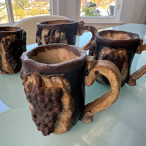 May include: Four brown and white ceramic mugs with unique textured designs. Each mug has a handle and a wide rim.