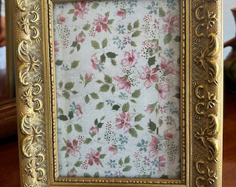 May include: A gold-colored picture frame with an ornate design. The frame is empty and ready to hold a photo or artwork.