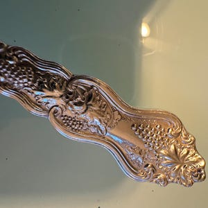 May include: A silver-plated fork with an ornate design featuring grapes and leaves.