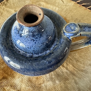 May include: A blue and brown ceramic oil lamp with a handle. The lamp has a round base and a spout for pouring oil.