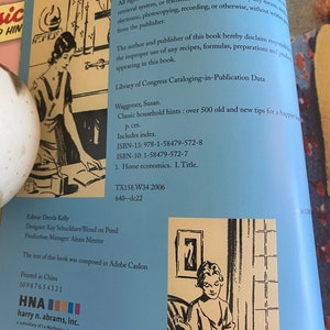 Pode incluir: Uma capa de livro com fundo azul e texto branco. O t&iacute;tulo do livro &eacute; "Classic Household Hints: Over 500 Old and New Tips for a Happier Home". A autora &eacute; Susan Waggoner. A capa do livro tamb&eacute;m apresenta uma ilustra&ccedil;&atilde;o em preto e branco de uma mulher sentada em uma cadeira.