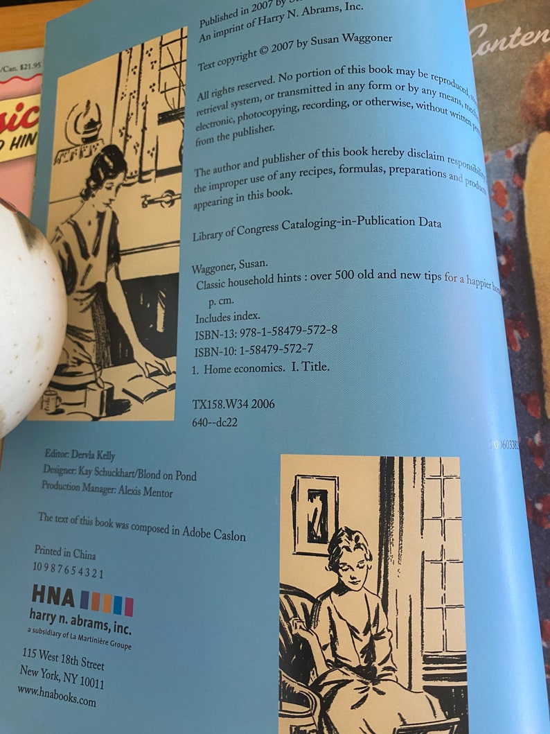 Pode incluir: Uma capa de livro com fundo azul e texto branco. O t&iacute;tulo do livro &eacute; "Classic Household Hints: Over 500 Old and New Tips for a Happier Home". A autora &eacute; Susan Waggoner. A capa do livro tamb&eacute;m apresenta uma ilustra&ccedil;&atilde;o em preto e branco de uma mulher sentada em uma cadeira.