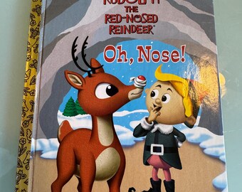 Op de afbeelding: Een kinderboek getiteld "Rudolph the Red-Nosed Reindeer" met de tekst "Oh, Nose!" op de cover. De cover toont een cartoon illustratie van Rudolph en een elf.