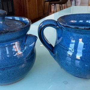 May include: A blue ceramic sugar bowl with a lid and a blue ceramic creamer.