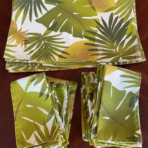 May include: A set of green and white tropical leaf patterned placemats and napkins. The placemats are stacked and the napkins are folded.