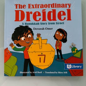 May include: A children's book titled "The Extraordinary Dreidel" with a blue background and illustrations of a dreidel, a boy, and a girl. The book is part of the PJ Library program and is a Hanukkah story from Israel.