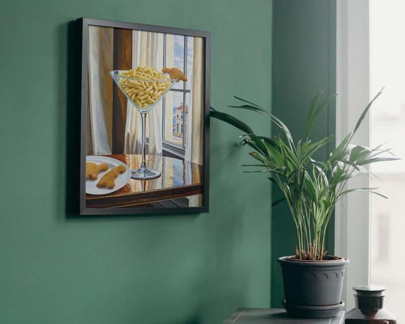 May include: A framed painting of a martini glass filled with crackers and a plate with two crackers on a wooden table. The painting is hanging on a green wall.
