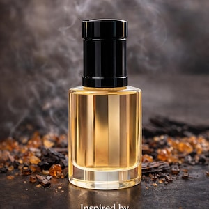 May include: A perfume bottle with a black cap and a golden liquid, labelled "Inspired by Ombre Nomad". The background is dark with a smoky effect and scattered amber crystals. The bottle has a rectangular shape.