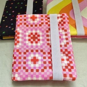 May include: Three rectangular fabric covers with elastic bands. The front cover features a pink, red, and white checkered pattern. The back left cover is black with multicolored stars, and the back right cover has yellow, orange, and pink waves.
