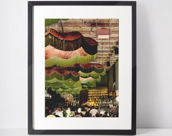 May include: A photograph of a restaurant interior with a ceiling decorated with green and brown fringed lampshades. The restaurant is filled with people and has a bar in the background.
