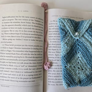 May include: A close-up of a book with a pink crocheted bookmark. The book is open to a page with text about Christian instruction. The bookmark is a crocheted pouch with a pearl button.