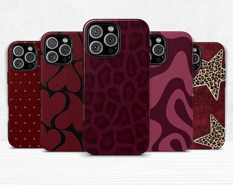 May include: A collection of five phone cases in varying designs and patterns. The cases are primarily burgundy, with patterns including polka dots, hearts, leopard print, wavy lines, and a star with a leopard print overlay. The cases are all the same size and shape.