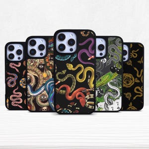 Könnte beinhalten: Eine Sammlung schwarzer Handyhüllen mit verschiedenen Designs, die Schlangen, einen Oktopus und andere Illustrationen zeigen. Die Hüllen zeigen eine Vielzahl von Farben, darunter Rot, Gelb, Grün und Lila. Die Hüllen sind in einer Reihe angeordnet, wobei die Kameralinsen sichtbar sind.