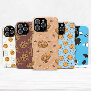 Puede incluir: Cinco fundas para teléfono con varios diseños. Una funda tiene un fondo amarillo claro con galletas y leche. Otra tiene un fondo marrón con galletas con chispas de chocolate. La tercera tiene un fondo beige con galletas y chispas de chocolate. La cuarta tiene un fondo azul con galletas. La última tiene un fondo azul con galletas y crema.