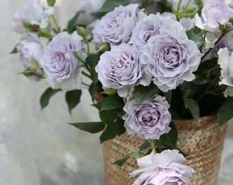 May include: A bouquet of lavender-colored roses in a woven basket. The roses are arranged in a loose, natural style, with some of the stems extending beyond the basket.