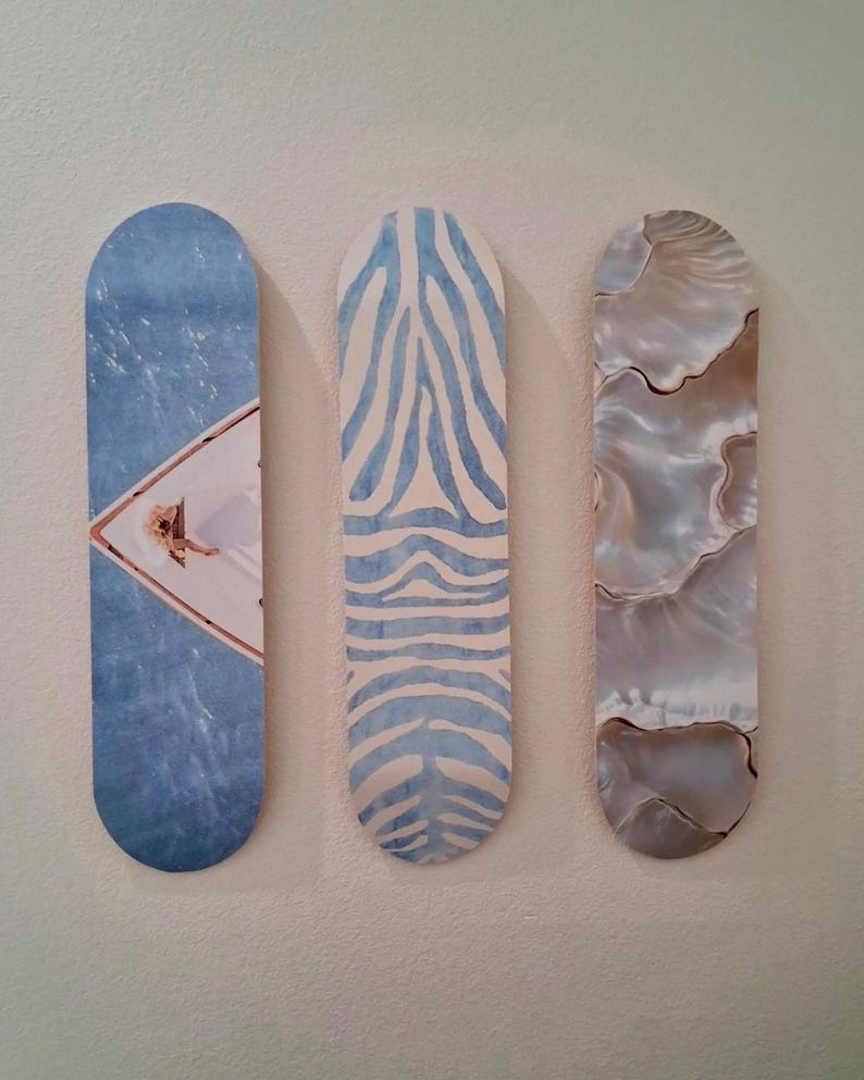 May include: Three decorative wall art pieces. The first is blue with a diamond-shaped image. The second has a blue and white zebra stripe pattern. The third has a pearlescent, marbled design in shades of gray and brown.