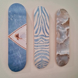 May include: Three decorative wall art pieces. The first features a blue water scene with a white boat. The second has a blue and white zebra stripe pattern. The third has a pearlescent, swirling design.
