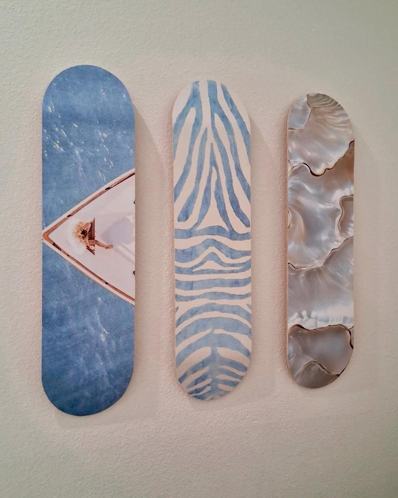 May include: Three decorative wall art pieces. The first features a blue water scene with a white boat. The second has a blue and white zebra stripe pattern. The third has a pearlescent, swirling design.