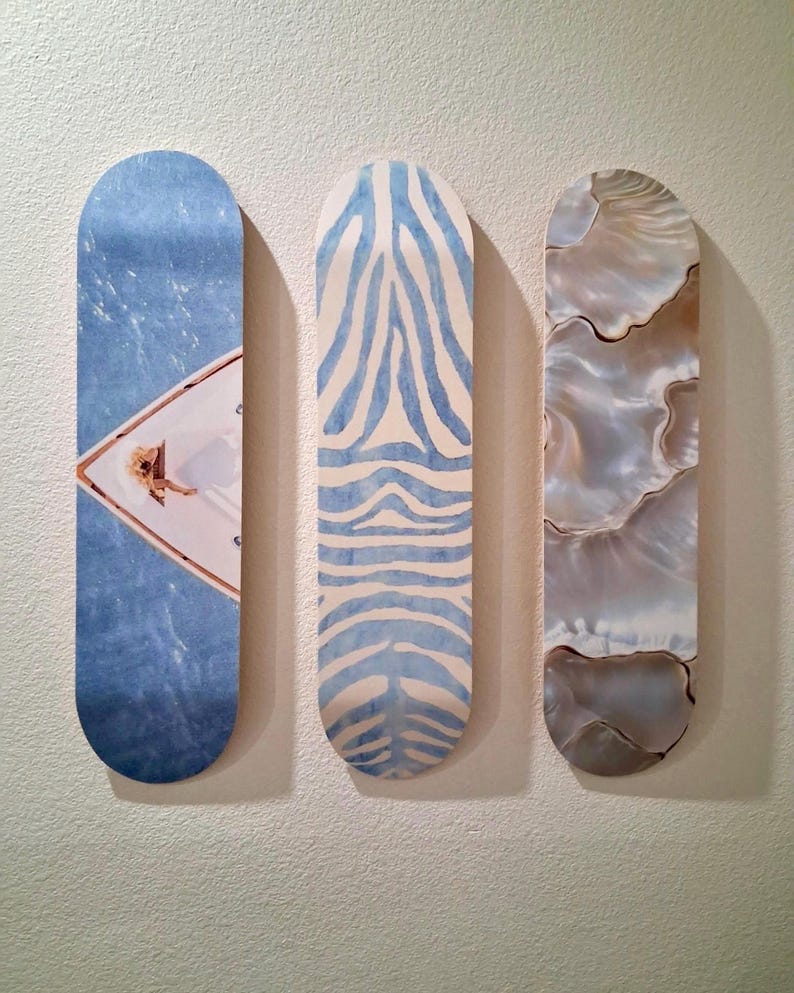 May include: Three skateboard decks with unique designs. One features a blue water scene with a person on a boat, another has a blue zebra stripe pattern, and the last has a pearlescent, shell-like design.