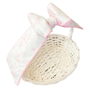 May include: A white wicker basket with a pink satin bow. The bow has a white and pink floral pattern.