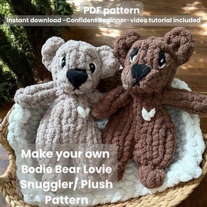 May include: Two crocheted bear plush toys, one light brown and one dark brown, with black noses and white heart accents. The bears are on a white blanket in a woven basket. Text on the image reads "PDF pattern" and "Make your own Bodie Bear Lovie Snuggler/ Plush Pattern."