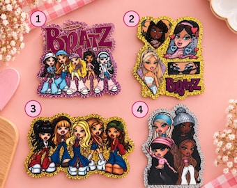 Könnte beinhalten: Vier glitzernde Acryl-Anhänger mit Bratz-Charakter-Illustrationen. Anhänger 1 hat violetten Glitzer und das Bratz-Logo. Anhänger 2 hat goldenen Glitzer und herzförmige Porträts. Anhänger 3 hat goldenen Glitzer und fünf Figuren. Anhänger 4 hat silbernen Glitzer.