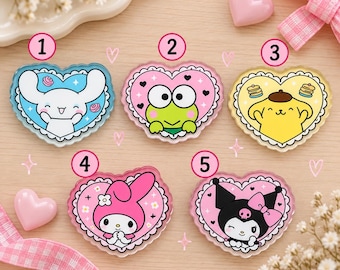 Könnte beinhalten: Fünf herzförmige Acryl-Anstecknadeln mit Sanrio-Figuren. Nummer 1 zeigt einen weißen Hund auf Blau, 2 einen grünen Frosch auf Pink, 3 einen gelben Hund auf Gelb, 4 einen rosa Hasen auf Pink und 5 eine schwarz-weiße Figur auf Pink.