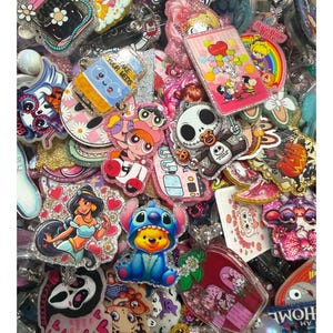 Puede incluir: Una colección de coloridos y brillantes carretes para insignias con varios personajes y diseños de dibujos animados. El surtido incluye imágenes de Jasmine, Stitch, Jack Skellington y las Supernenas, entre otros. Los carretes para insignias tienen una variedad de formas y tamaños.