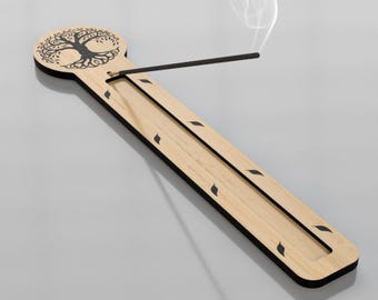 May include: A wooden incense holder with a tree of life design. The holder is rectangular with a light wood finish and black trim. An incense stick is lit, with smoke rising. The design includes leaf-shaped cutouts along the sides.
