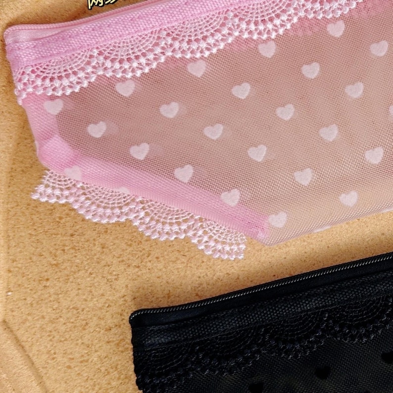 May include: Close-up of pink and black underwear. The pink underwear features a delicate lace trim and a sheer fabric dotted with white hearts. The black underwear has a lace trim along the top edge.