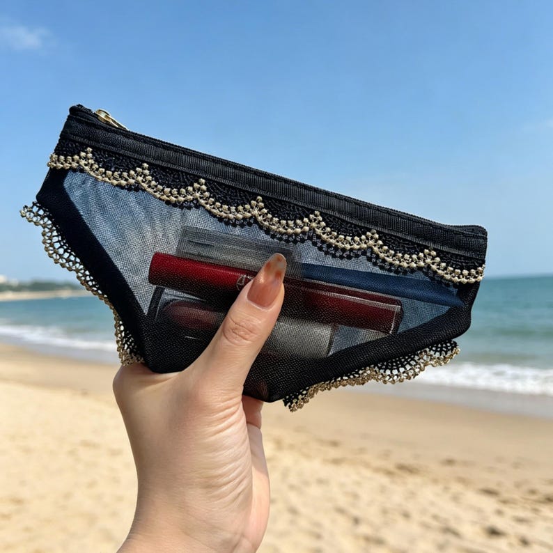 May include: Black mesh cosmetic bag with gold trim and a gold zipper. The bag is filled with lipsticks and other makeup items. The bag is held up against a beach background.