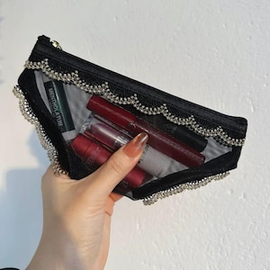 May include: Black mesh cosmetic bag with a decorative silver trim and a gold zipper. The bag contains several lipsticks and a tube of "MENTHOLATUM". The bag is held in a hand.