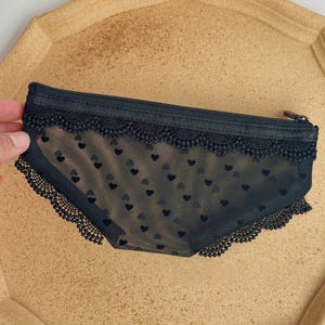 May include: Black lingerie-style pencil case with a zipper closure. The case is made of sheer black fabric with a heart pattern and lace trim along the top and bottom edges. The case is approximately 8 inches long.
