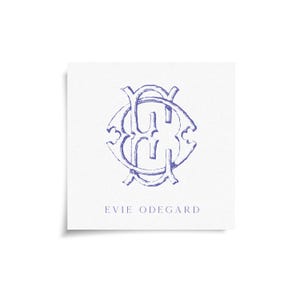 May include: A square card with a blue monogram design and the name "EVIE ODEGARD" printed below. The monogram is an intricate, overlapping design with a vintage aesthetic, set against a white background.