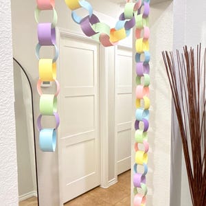 May include: A colorful paper chain garland in pastel shades of pink, blue, yellow, and green hangs from a doorway. The chain is made of interlocking paper loops, creating a festive and decorative element. The garland adds a touch of whimsy to the interior space.