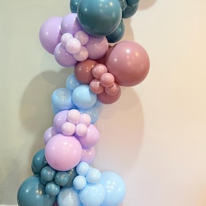 May include: A vertical balloon garland in shades of blue, pink, and mauve. The arrangement features various sizes of balloons, creating a textured and layered effect. Ideal for party decorations or event backdrops.