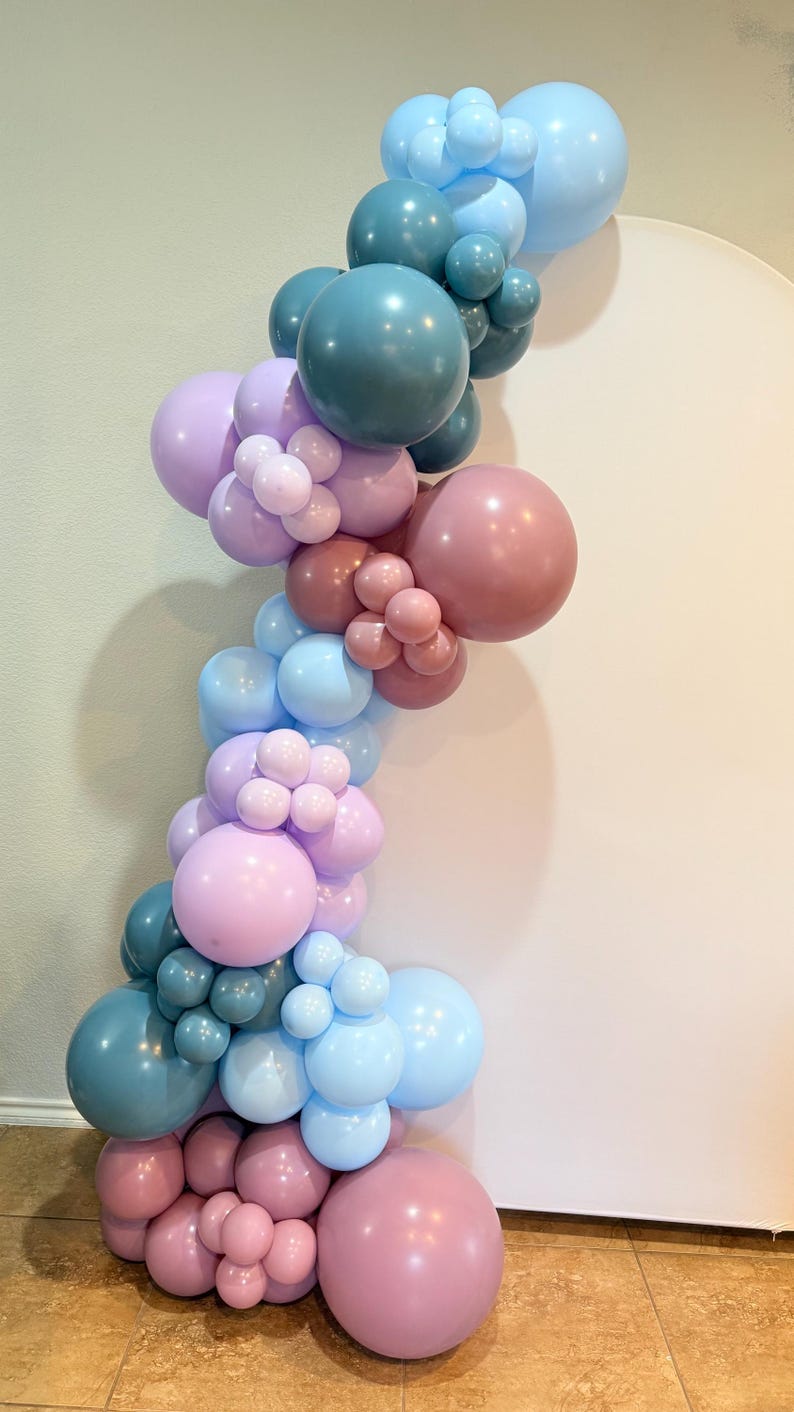 May include: A vertical balloon garland in shades of blue, pink, and mauve. The arrangement features various sizes of balloons, creating a textured and layered effect. Ideal for party decorations or event backdrops.