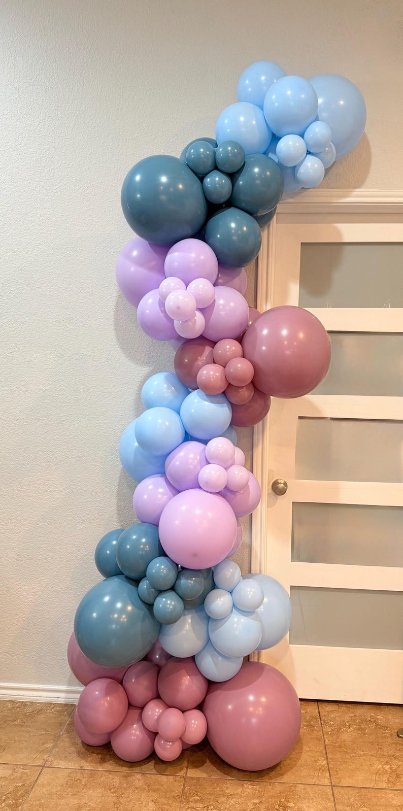 May include: A balloon arch in shades of blue, lavender, and mauve, arranged in a cascading design. The balloons vary in size, creating a textured and visually appealing display. Perfect for a party or event.