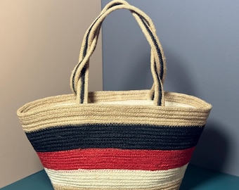 May include: A striped tote bag made of woven rope. The bag has black, red, and white stripes. The bag has two rope handles.