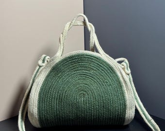 May include: A green and white striped round straw bag with a top handle and a long shoulder strap.
